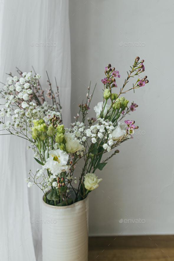 Modern bouquet in vase against tulle and rustic wall Stock Photo