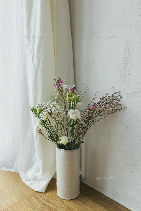 Modern bouquet in vase against tulle and rustic wall. Stylish