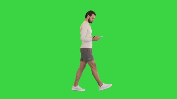 Male Runner Walking and Typing Something on His Mobile Smart Phone on a Green Screen Chroma Key alt