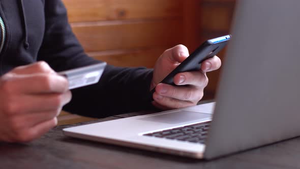 Businessman in a Black Hoodie Making Online Payment with Credit Card and Smartphone Online Shopping alt