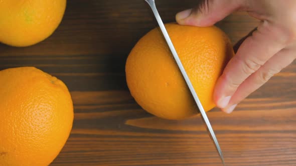 Male hand with big knife slicing orange citrus fruit on the cutting board at kitchen
