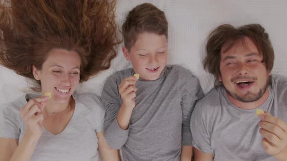 Happy Family Adult Parents Mum Dad and Cute Little Boy Watching Tv Together Eat Snack Enjoy alt