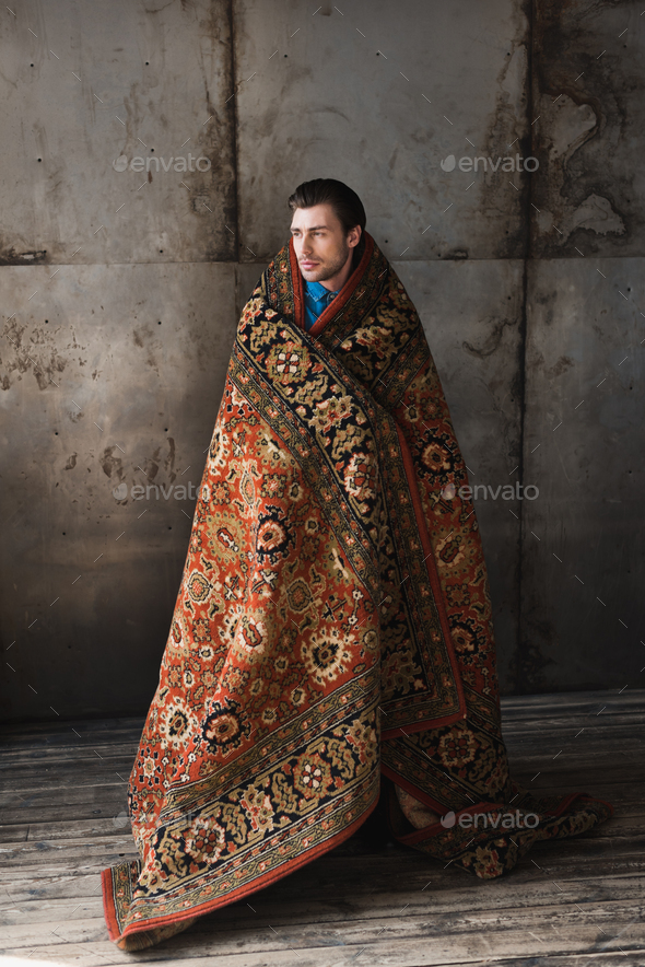 handsome young man covered in rug in front of concrete wall