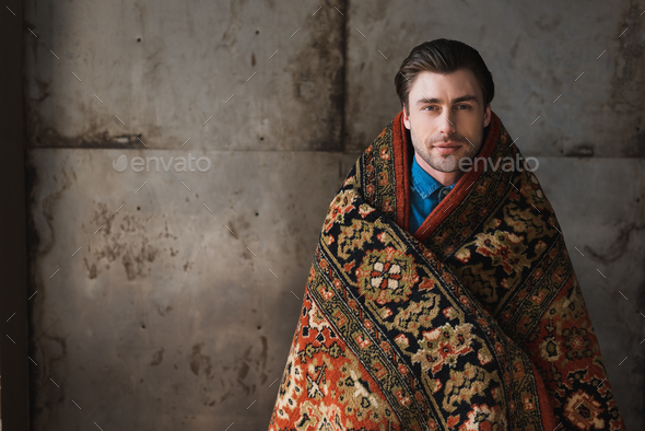 handsome young man covered in rug in front of concrete wall
