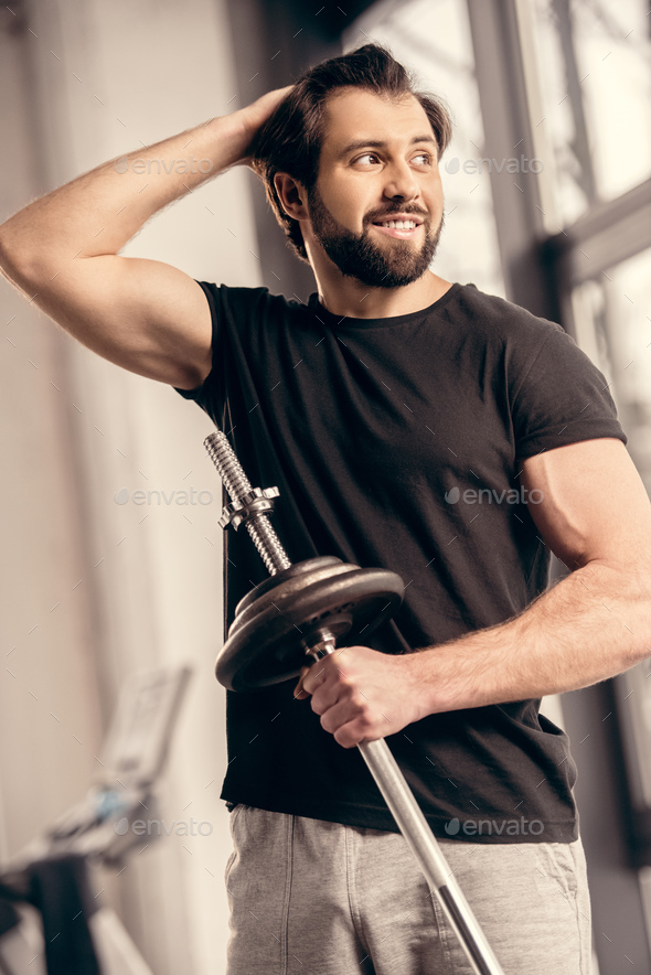 smiling sportsman holding iron bar and touching hair in gym Stock Photo