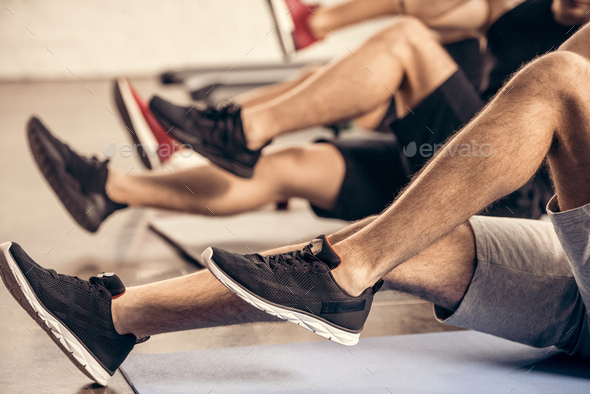 cropped image of sportsmen doing sit ups together in gym
