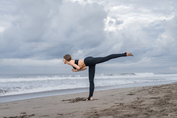 Warrior III yoga pose performed by fitness woman at beach stock photo