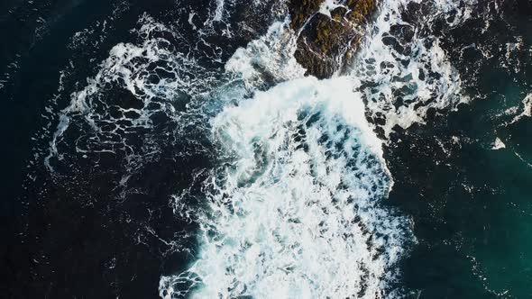Sea waves with sea foam hit the rocky shore. Aerial cinematic top view.