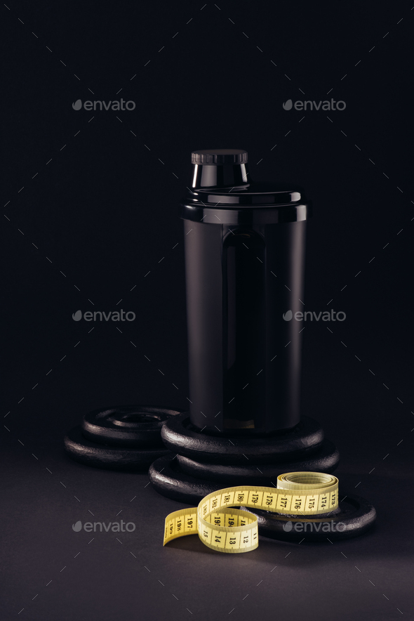 protein container with measuring tape and weight plates isolated on black