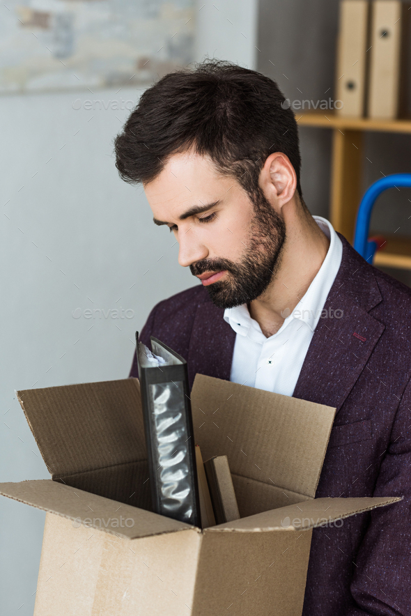 close-up shot of depressed young businessman with box of personal stuff after he gets fired