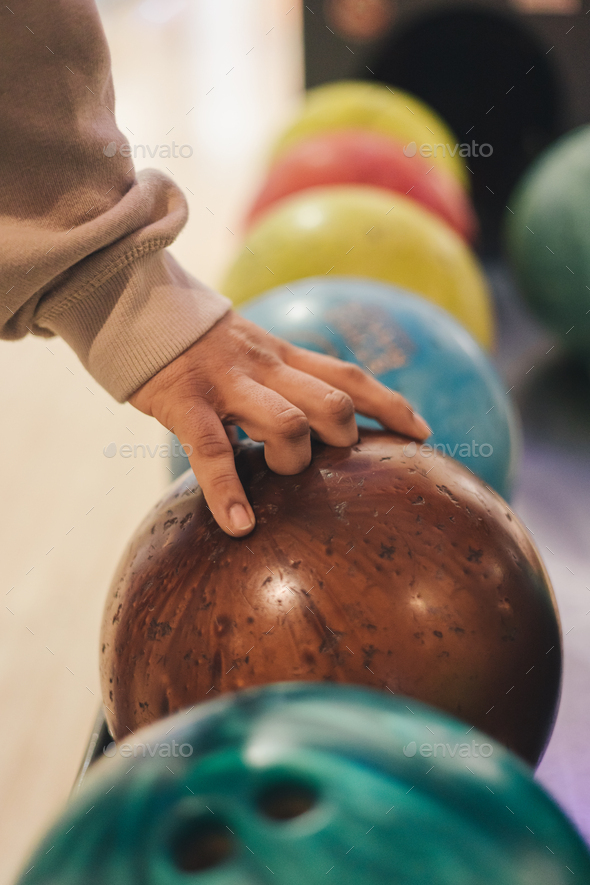 Cropped image of man\'s hand picking up brown bowling ball from rack