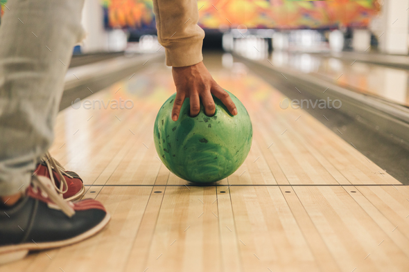 Man\'s hand holding a green bowling ball ready to throw it