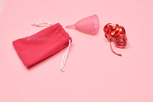 Pink menstrual cup on pink background. Decorated with red ribbon.
