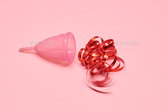 Pink menstrual cup on pink background. Decorated with red ribbon.