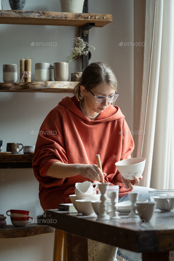 Focused artisan girl works on manufacture of clay ceramic products in potter studio for custom order
