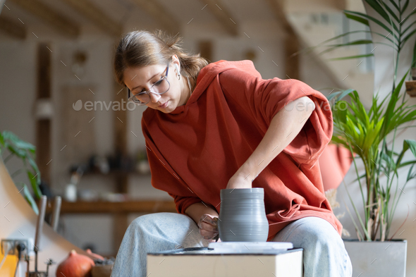 Creative successful woman attends pottery courses learns how to make craft dishes sits in workshop