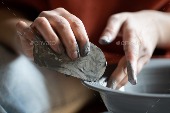 Hands of crafts woman shaping clay vessel with scraper during production of author dishes for sale