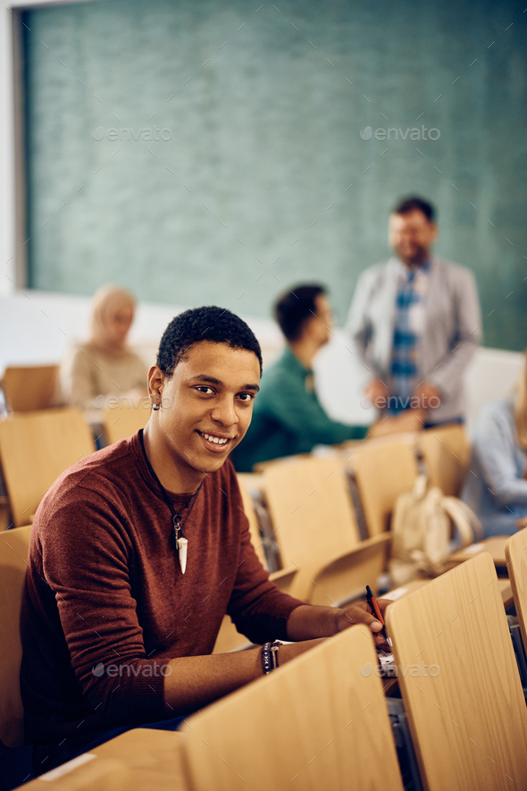 Happy black student attending a class at the university and looking at camera.