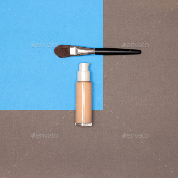 Makeup foundation bottle with make-up brush on blue and brown background, flat lay