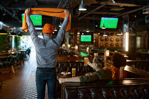 Young excited overjoyed friends watching football match in sports bar
