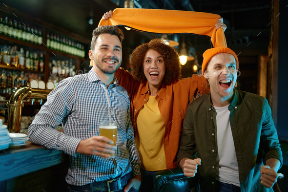 Excited diverse millennial friends gather in bar to watch football match