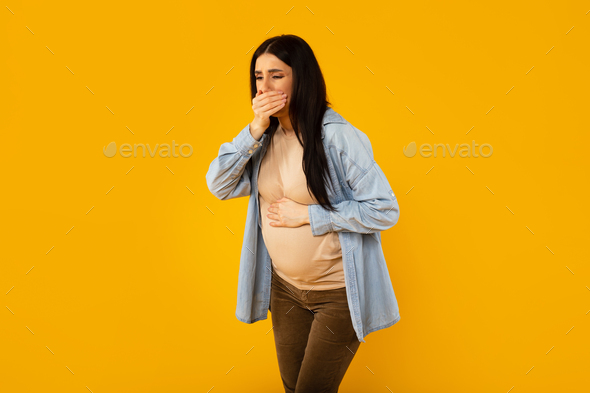 Pregnancy morning sickness. Young pregnant woman suffering from nausea, holding hand near mouth