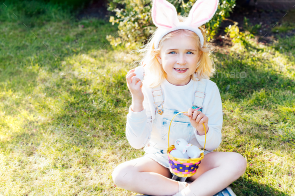 Portrait of happy little girl wearing bunny ears holding Easter egg after festive egg hunting
