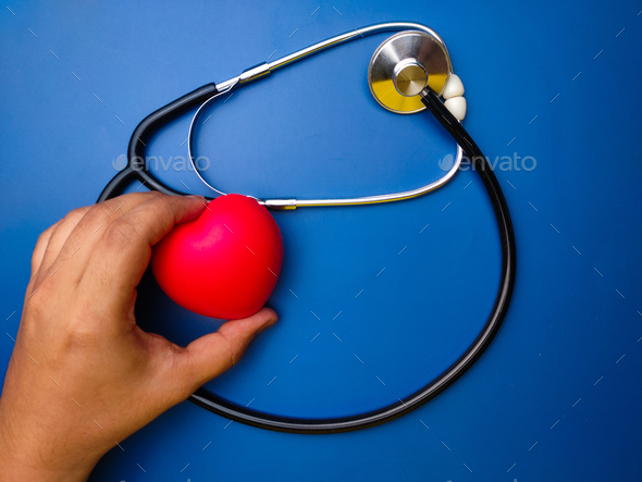 Hand holding red heart with statehoscop on blue background. Healthcare and medical concept. - Stock Photo - Images