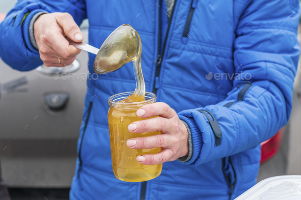 A man pours liquid bee honey into a jar. Sale of natural food