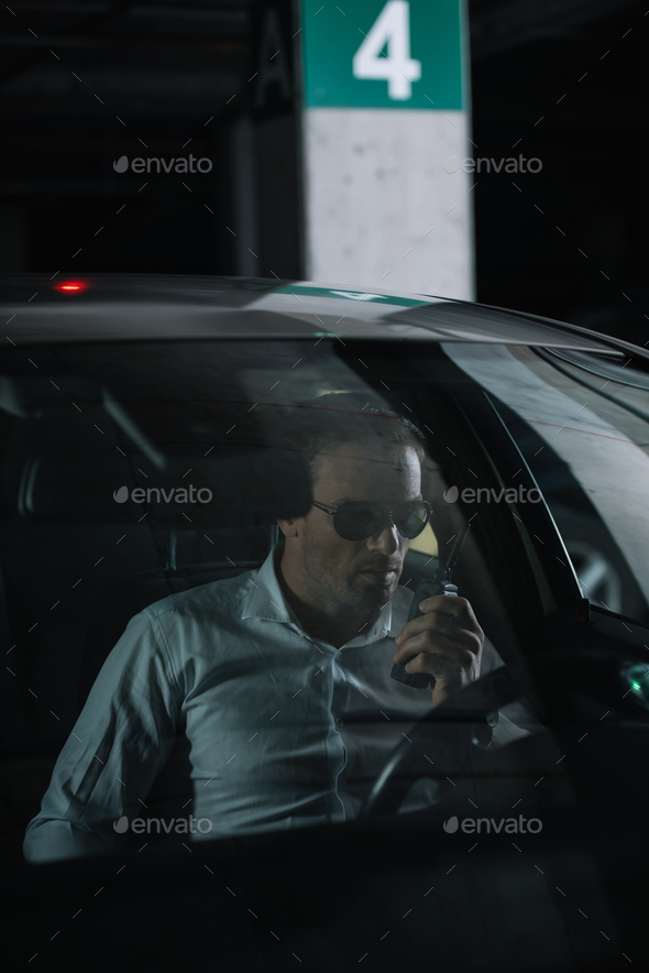 male undercover agent in sunglasses doing surveillance and using talkie  walkie in car Stock Photo by LightFieldStudios