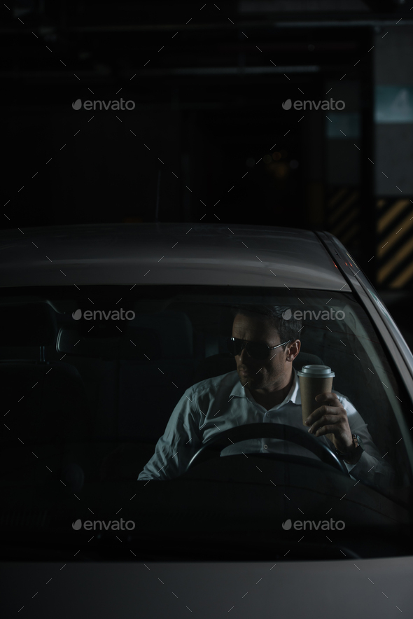 male undercover agent in sunglasses sitting in car with paper cup