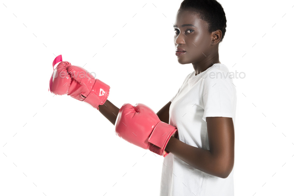 side view of african american woman in pink boxing gloves looking at camera isolated on white,
