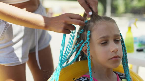 A Girl in a Suit Weaves African Braids in Her Hair on a Sunny Day alt