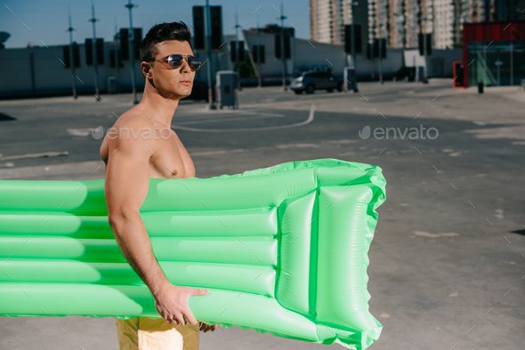 attractive young shirtless man with inflatable bed on parking