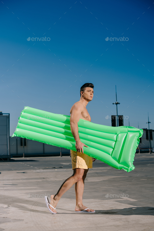 handsome young shirtless man with inflatable bed on parking