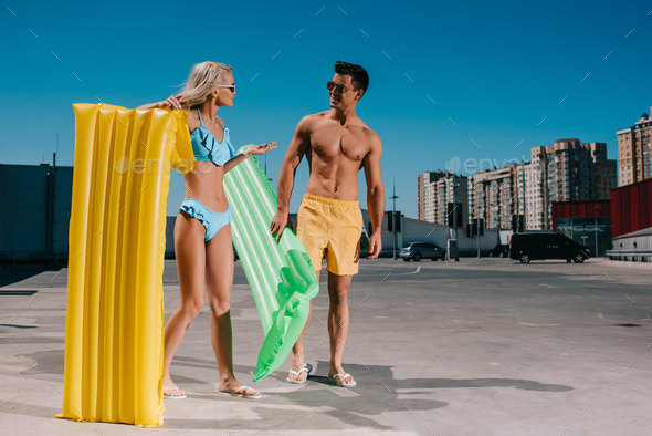 attractive young couple in beach clothes with inflatable beds on parking