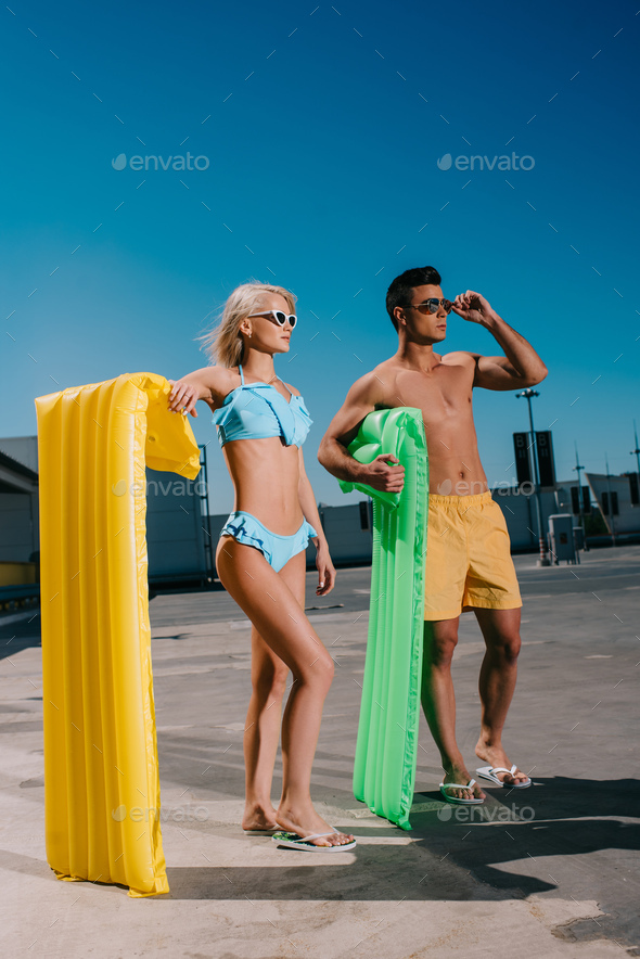 young couple in beach clothes with inflatable beds standing on parking