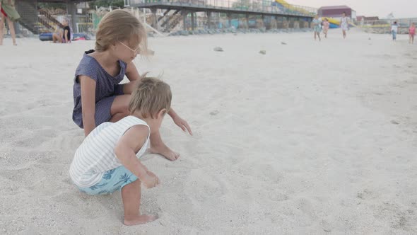 Girl Helping Her Little Brother to Look for Seashells in the Sand on the Coast alt