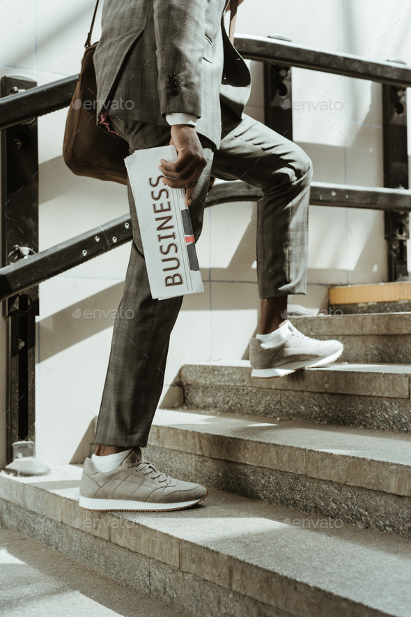 Cropped view of african american businessman with newspaper walking on stairs