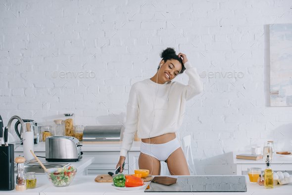beautiful young woman listening music with earphones and preparing breakfast
