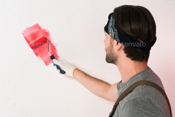 back view of man in headband painting wall in red by paint roller