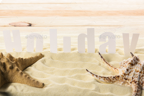 Starfish with seashell and Holiday inscription on sandy beach