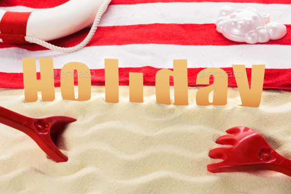 Beach toys and towel with Holiday inscription on sandy beach