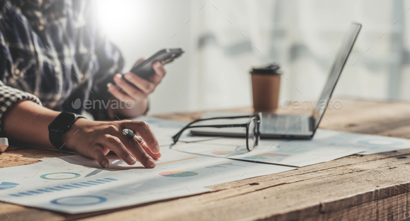 Young accountant hand holding smartphone to call marketing consultants and using laptop computer to