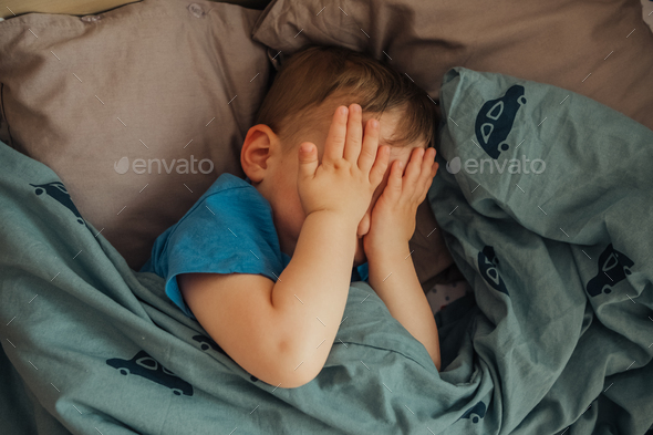 Close up on single boy rubbing his eyes with both hands while he is in bed for sleeping