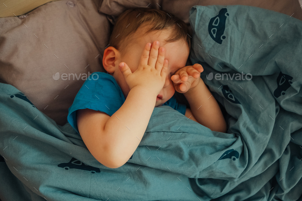 Close up on single boy rubbing his eyes with both hands while he is in bed for sleeping