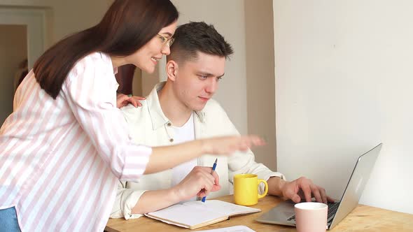 Young Cheerful Couple Uses a Laptop to Work Remotely on the Internet alt