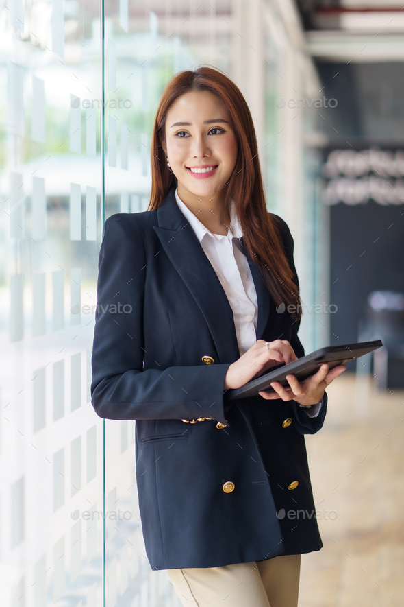 Attractive Asian business woman stand at work happily working using tablet at office
