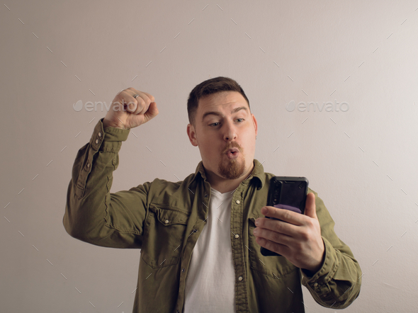 Middle-aged Caucasian male holding smartphone feeling euphoric with mobile online bet bid game win