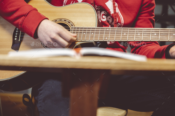 Person playing the guitar with note sheets on the table under the lights
